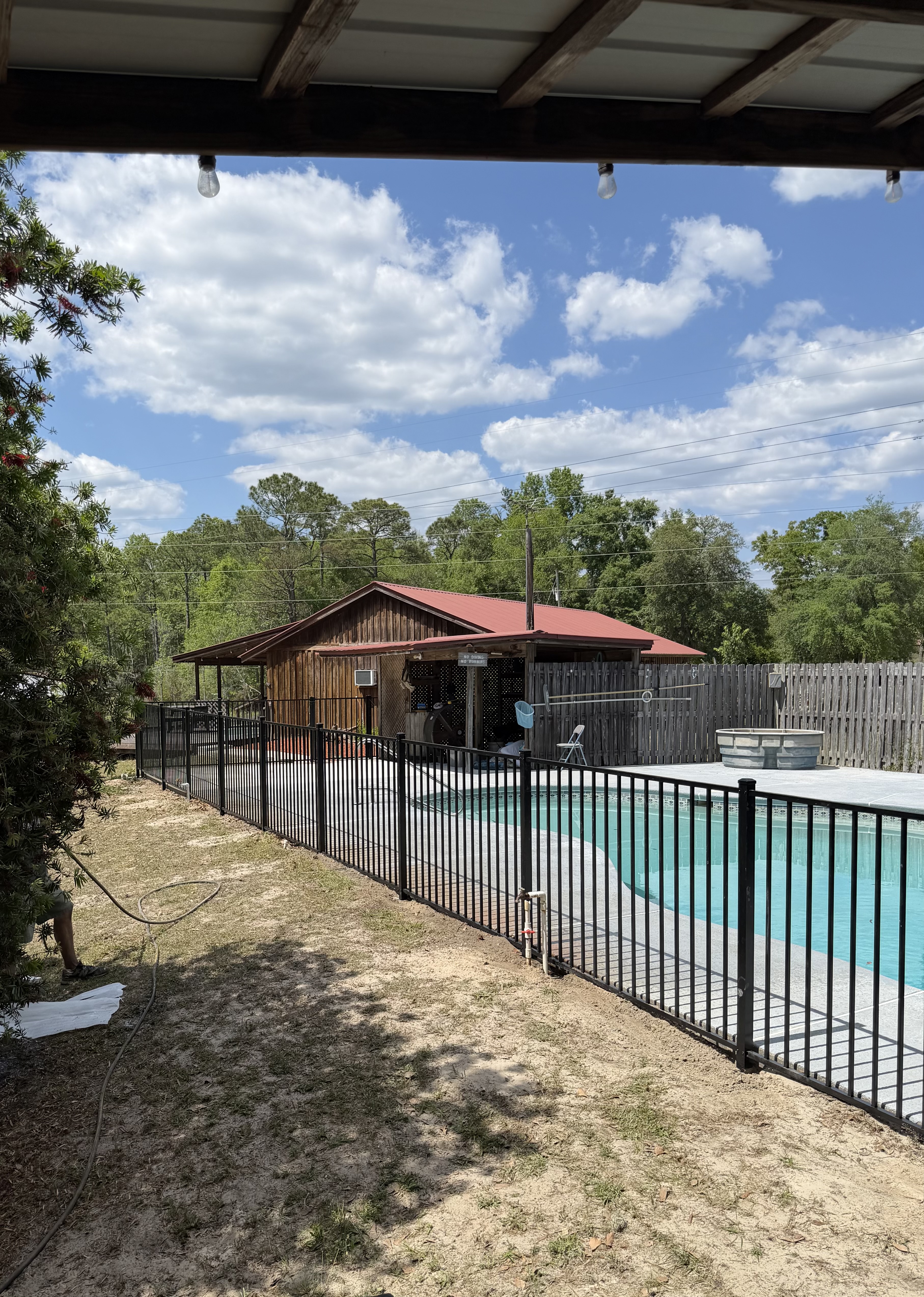 Black aluminum pool fence enclosing an in-ground swimming pool and concrete deck