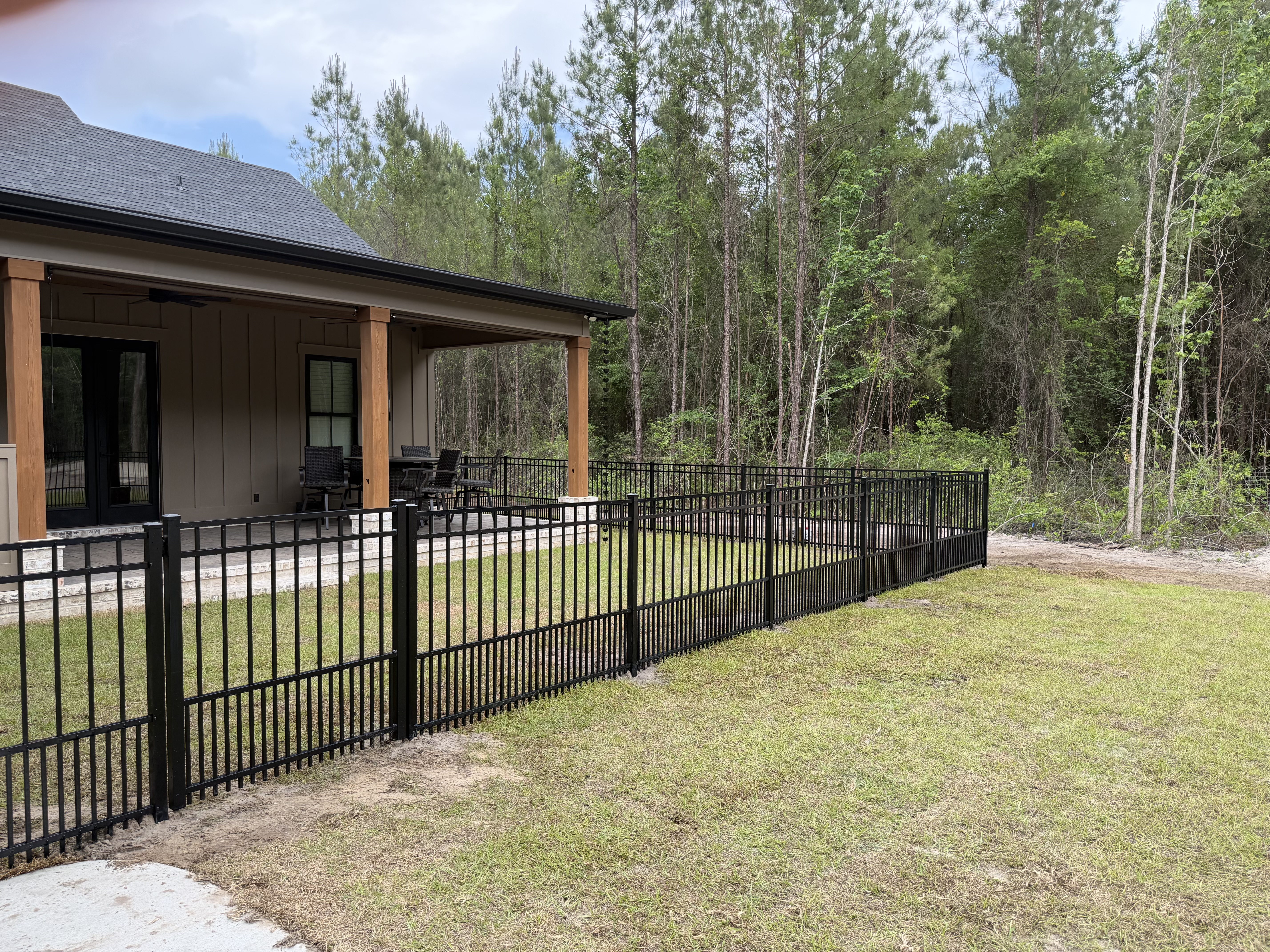 Black aluminum fence enclosing the covered patio and lawn of a residential home at the tree line