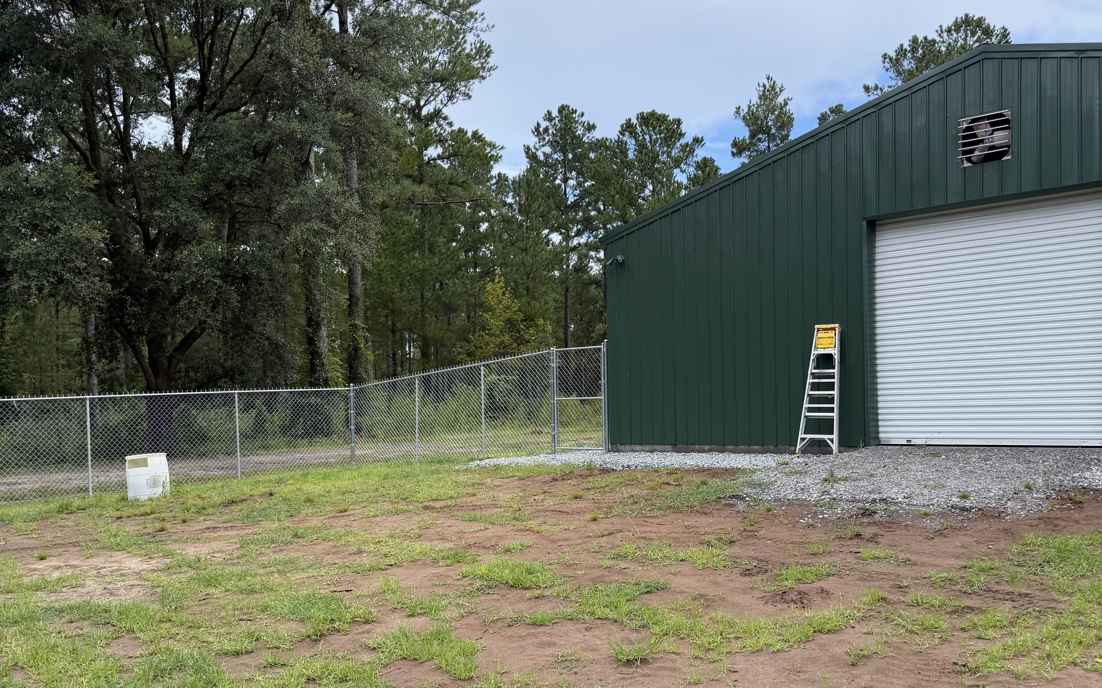 Galvanized chain-link fence line running beside a large green metal building on a cleared property
